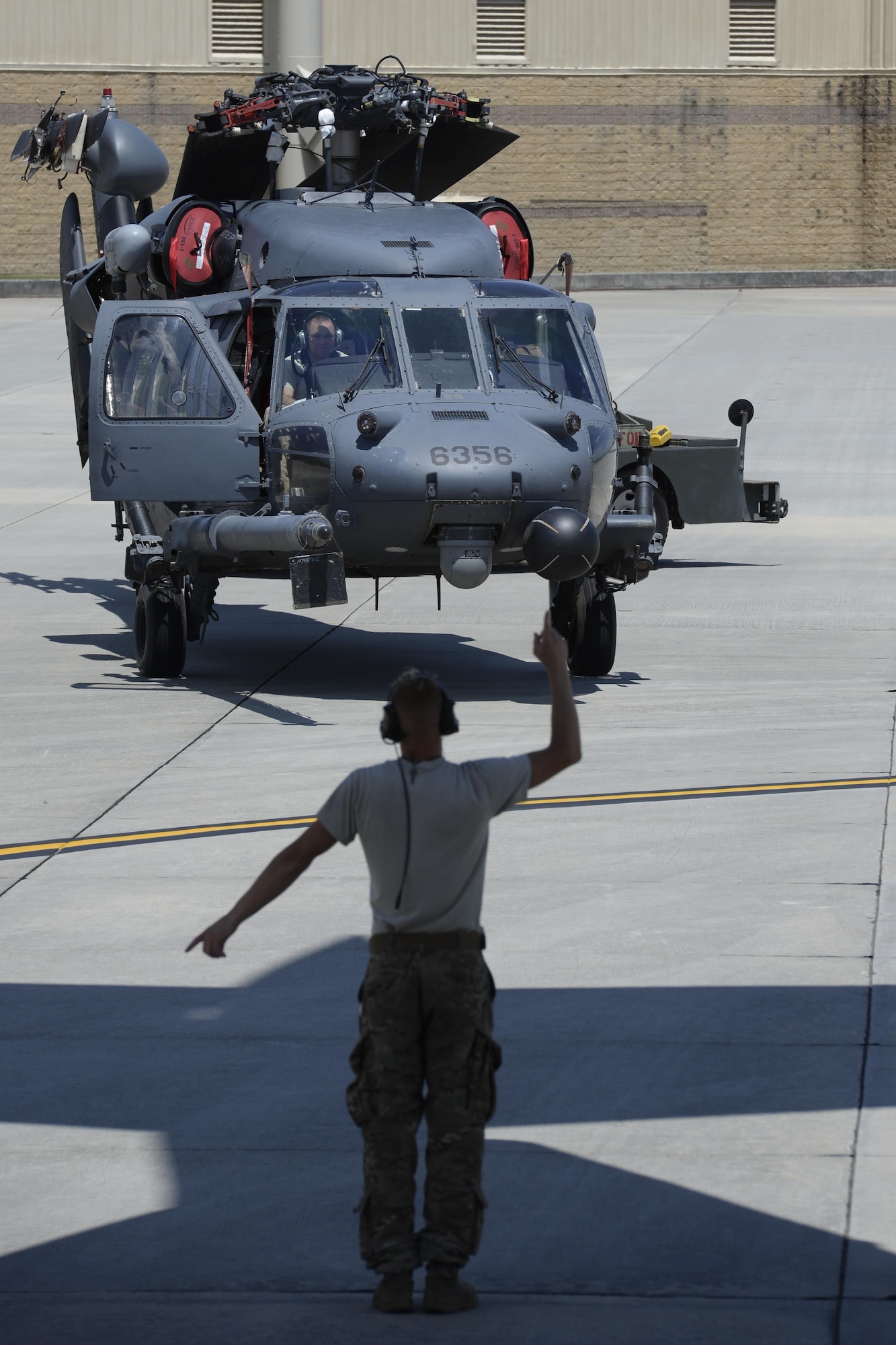 A member of the 723d Aircraft Maintenance Squadron, 41st Helicopter Maintenance Unit assigned to Moody Air Force Base, Ga., marshals an HH-60G Pave Hawk search and rescue helicopter toward a 3d Airlift Squadron C-17 Globemaster III May 15, 2017, at Moody AFB. Loading the helicopter required the use of vehicles, a winch and about 10 Airmen pushing, pulling and steering. (U.S. Air Force photo by Senior Airman Aaron J. Jenne)