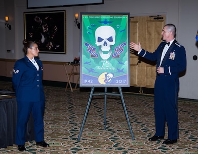 Senior Airman Destiny Lemos, 92nd Cyberspace Operations Squadron, and Lt Col Benjamin Montgomery, 92nd COS commander, unveil the 92nd COS 75th Anniversary poster commemorating the squadron's lineage from air warfare to cyber warfare during a Dining Out ceremony May 12, 2017, at Joint Base San Antonio-Lackland.