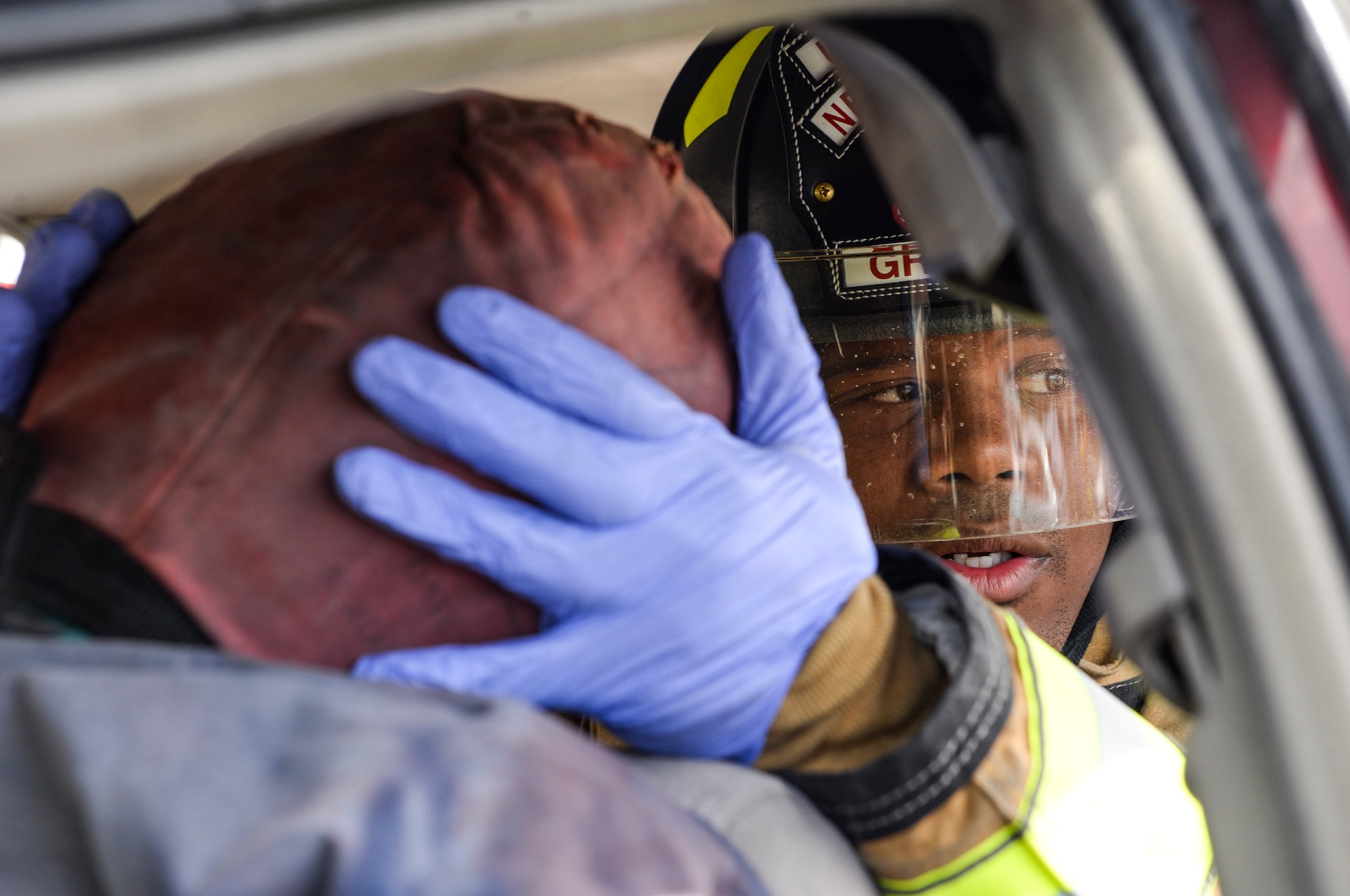 A firefighter from the 99th Civil Engineer Squadron stabilizes the head of a simulated car crash victim at Nellis Air Force Base, Nev., May 17, 2017. The simulation required vehicle operators from the 99th Logistics Readiness Squadron to flip an overturned vehicle. Firefighters then arrived on scene to evacuate the driver by cutting the roof off the crashed vehicle. (U.S. Air Force photo by Airman 1st Class Andrew D. Sarver/Released)