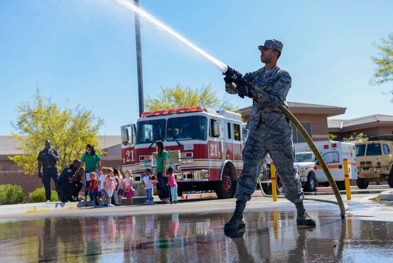 Airman 1st Class Michael Tuck, 99th Civil Engineer Squadron firefighter, shoots water out of a firehose at the child development center at Nellis Air Force Base, Nev., May 16, 2017. The display was part of the Touch-A-Truck event for National Defense Transportation Week. (U.S. Air Force photo by Airman 1st Class Andrew D. Sarver/Released)