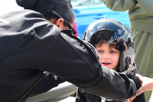 U.S. Air Force Tech. Sgt. Darshele Green, F-22 Raptor Demonstration Team avionics specialist, assists a child while he tries on a pilot’s helmet during the 911th Airlift Wing's Wings Over Pittsburgh 2017 Air Show, at Coraopolis, Pa., May 13, 2017. Throughout the show, the demonstration team hosted a tent for spectators to visit and talk with members the team. (U.S. Air Force/Senior Airman Kimberly Nagle)