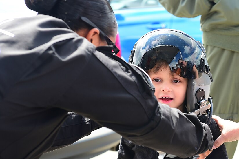 U.S. Air Force Tech. Sgt. Darshele Green, F-22 Raptor Demonstration Team avionics specialist, assists a child while he tries on a pilot’s helmet during the 911th Airlift Wing's Wings Over Pittsburgh 2017 Air Show, at Coraopolis, Pa., May 13, 2017. Throughout the show, the demonstration team hosted a tent for spectators to visit and talk with members the team. (U.S. Air Force/Senior Airman Kimberly Nagle)