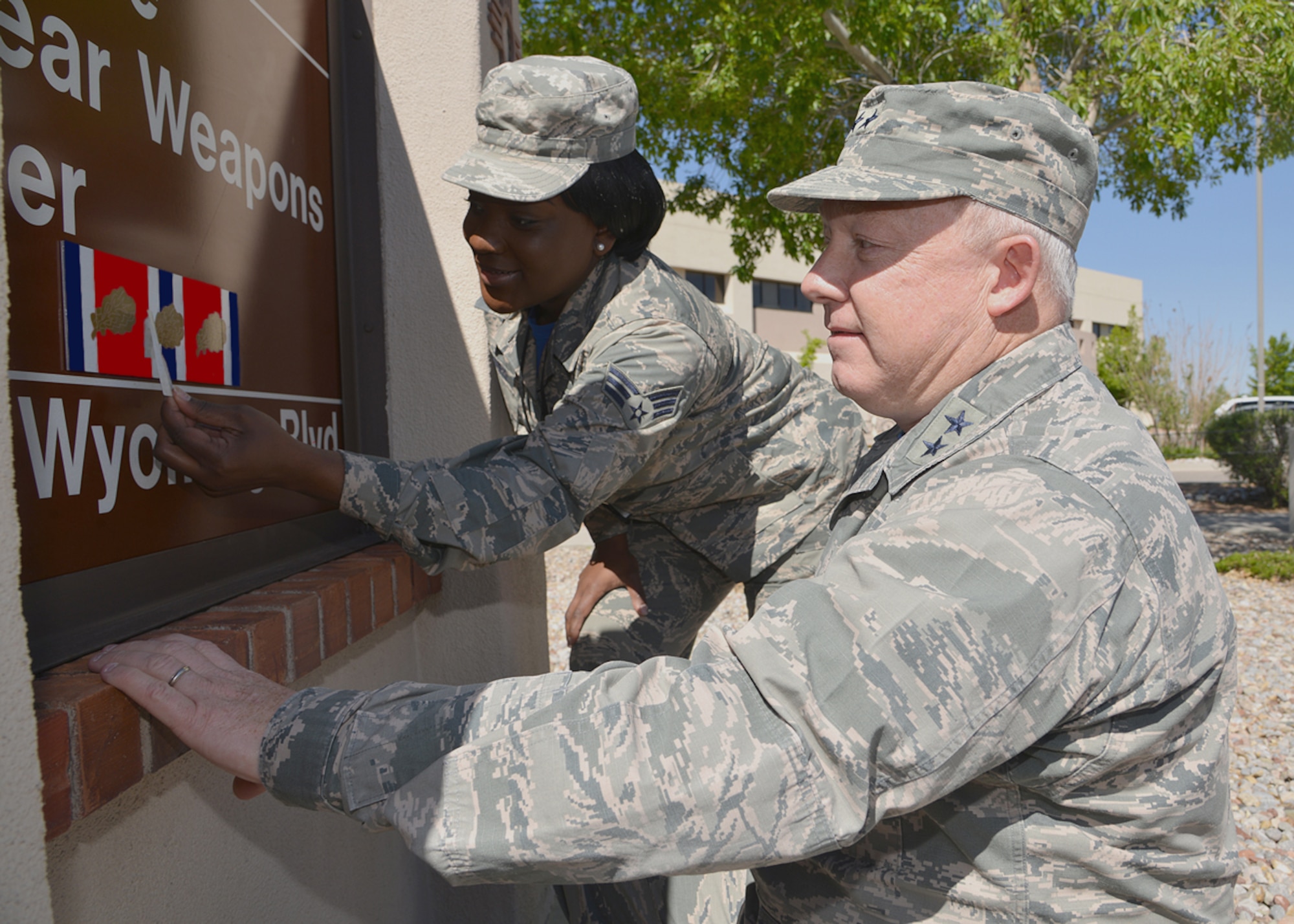 Maj. Gen. Scott W. Jansson, Air Force Nuclear Weapons Center commander and its most senior member, and Senior Airman Mychavia T. Harris, the center’s most junior member in 2015, affix the third oak leaf cluster to the Air Force Organizational Excellence Award ribbon on the AFNWC headquarters’ sign at Kirtland AFB, New Mexico.  The center was recognized for its 2015 achievements and accomplishments in nuclear materiel management in support of the nuclear deterrence mission. 
