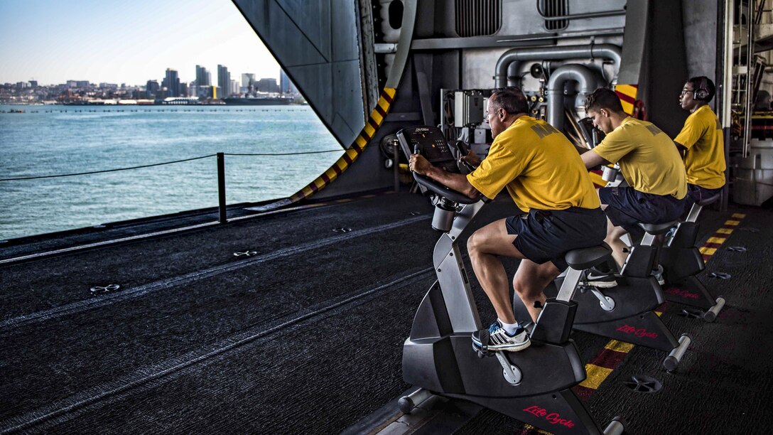 Sailors conduct their biannual physical readiness test on stationary bikes in the hangar bay of the aircraft carrier USS Theodore Roosevelt as the ship is moored pier-side in San Diego, May 22, 2017. Navy photo by Seaman Bill M. Sanders