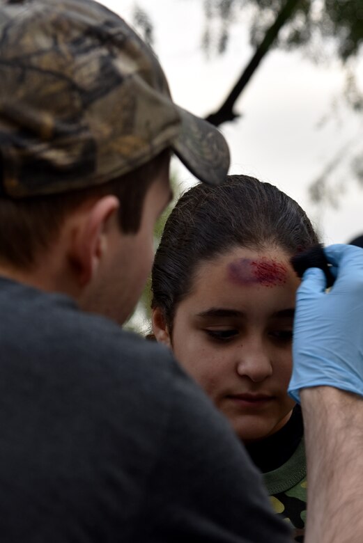 U.S. Air Force Senior Airman Joshua Cash, 17th Comptrollers Squadron customer service, paints fake wounds on to Olivia Akkurt, Operation: Kids Investigating Deployed Services deployer, during Operation: K.I.D.S. at Camp Sentinel on Goodfellow Air Force Base, Texas, May 20, 2017. Operation: K.I.D.S. is an annual event designed to introduce military children to deployment operations that their parents may experience. (U.S. Air Force photo by Staff Sgt. Joshua Edwards/Released)