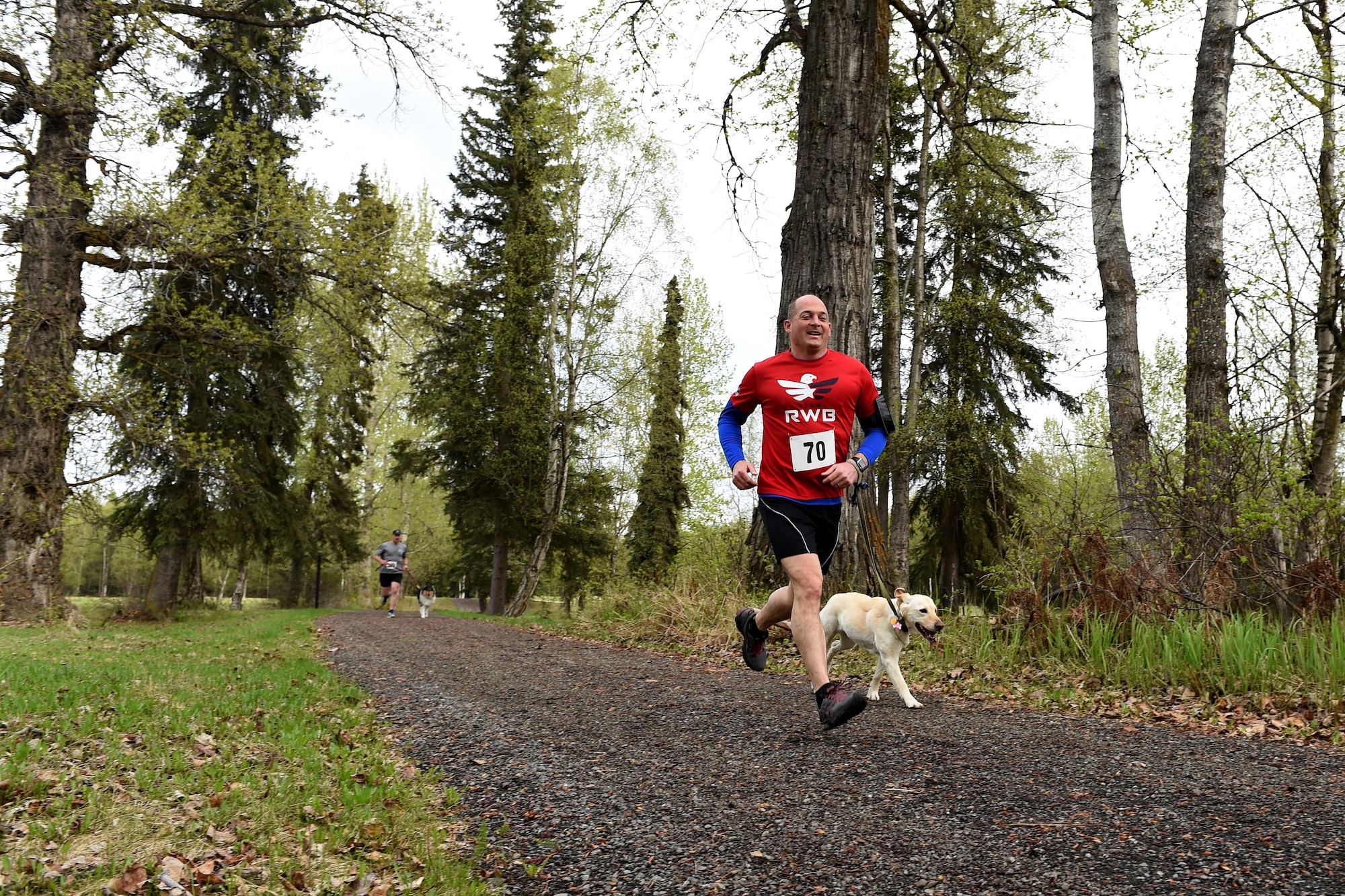 Air Force Col. George T.M. Dietrich III, Joint Base Elmendorf-Richardson and 673d Air Base Wing commander, and his dog, Aggie, race past Pet Fun Run 5K competitors at Eagleglen Fitness Park, at Joint Base Elmendorf-Richardson, Alaska, May 19, 2017. More than 40 athletes raced with their canine companions at the fun run. First, second and third place finishers received prizes, though all pets were given goodie bags. 