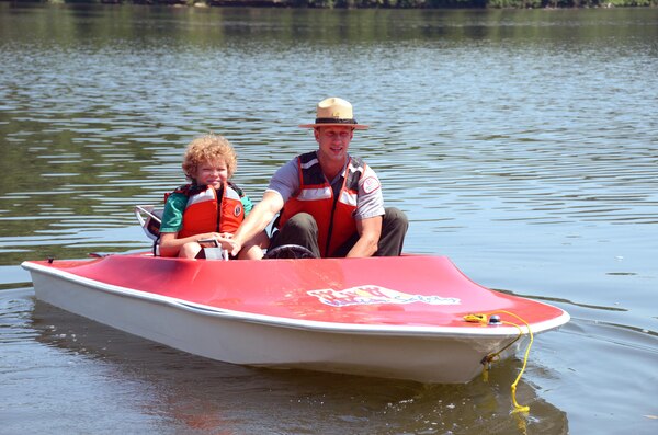A U.S. Army Corps of Engineers park ranger takes a camper on a boat ride. They are both playing it safe and wearing their personal flotation device.