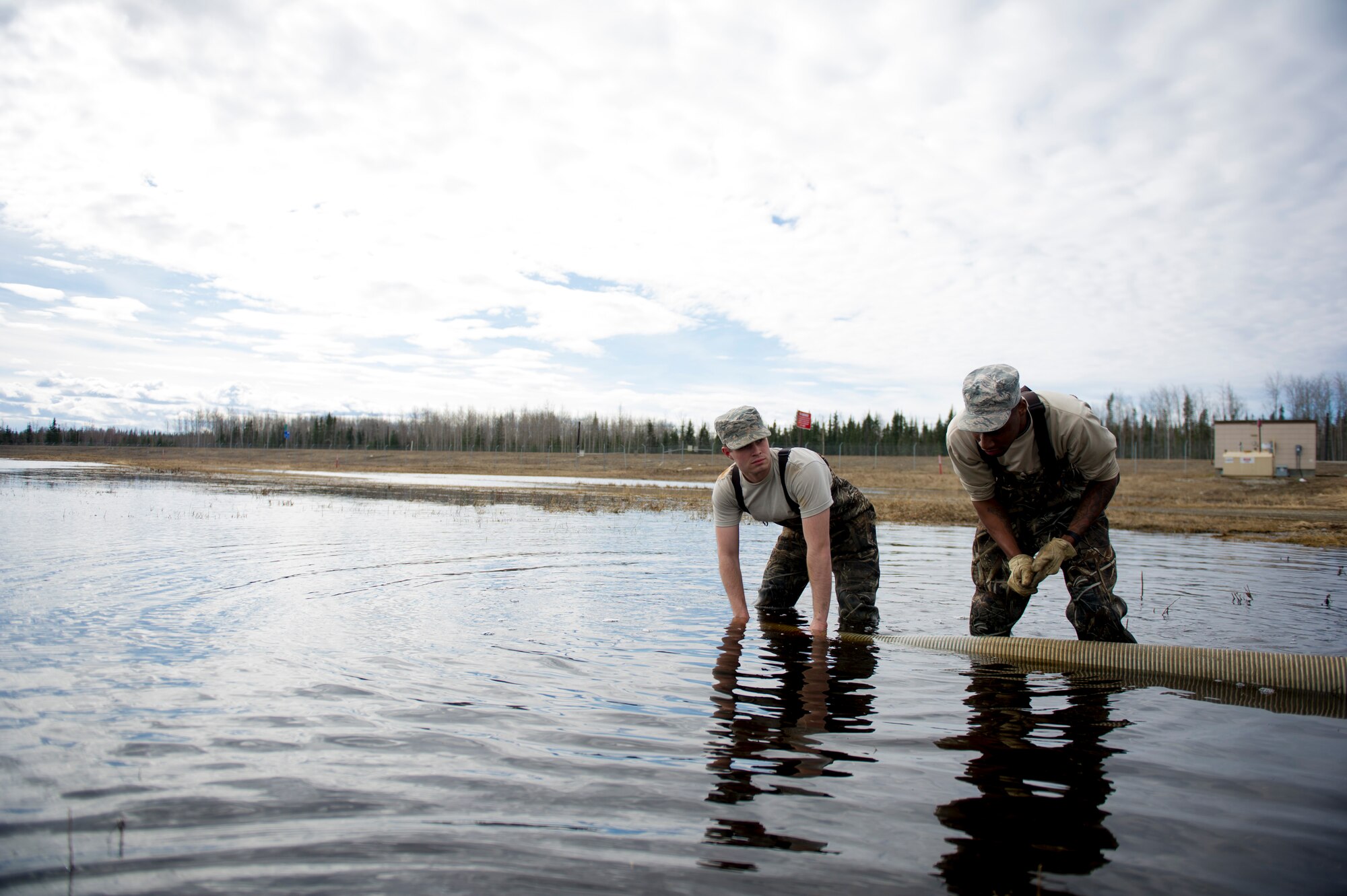 U.S. Air Force Airman 1st Class Augustus Hawkins, a 354th Civil Engineer Squadron pavement and construction equipment operator, submerges a hose in a pool of water April 10, 2017, at Eielson Air Force Base, Alaska. When the snow starts to melt water pools up on different areas of the base and has to be pumped to prevent potential damage to infrastructure. (U.S. Air Force photo by Airman 1st Class Isaac Johnson) 