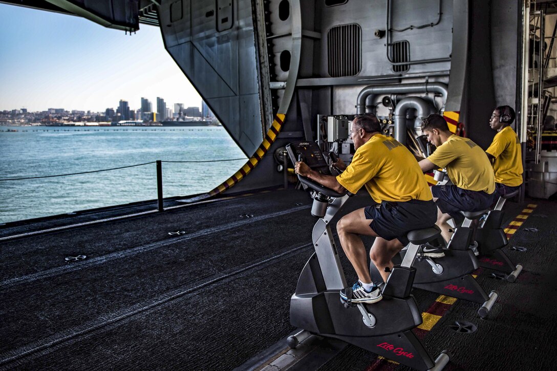 Sailors conduct their biannual physical readiness test on stationary bikes in the hangar bay of the aircraft carrier USS Theodore Roosevelt as the ship is moored pier-side in San Diego, May 22, 2017. Navy photo by Seaman Bill M. Sanders