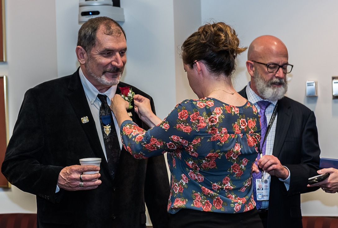 Michael Souders gets a flower pinned on by Protocol Officer Kristin Molinaro before the 2017 DLA Land and Maritime Hall of Fame induction ceremony begins.