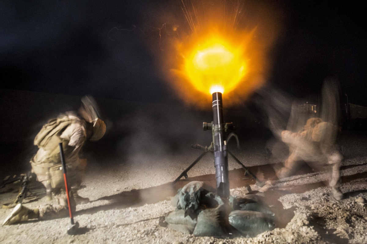 Marines fire an illumination mortar round at night on an airfield.