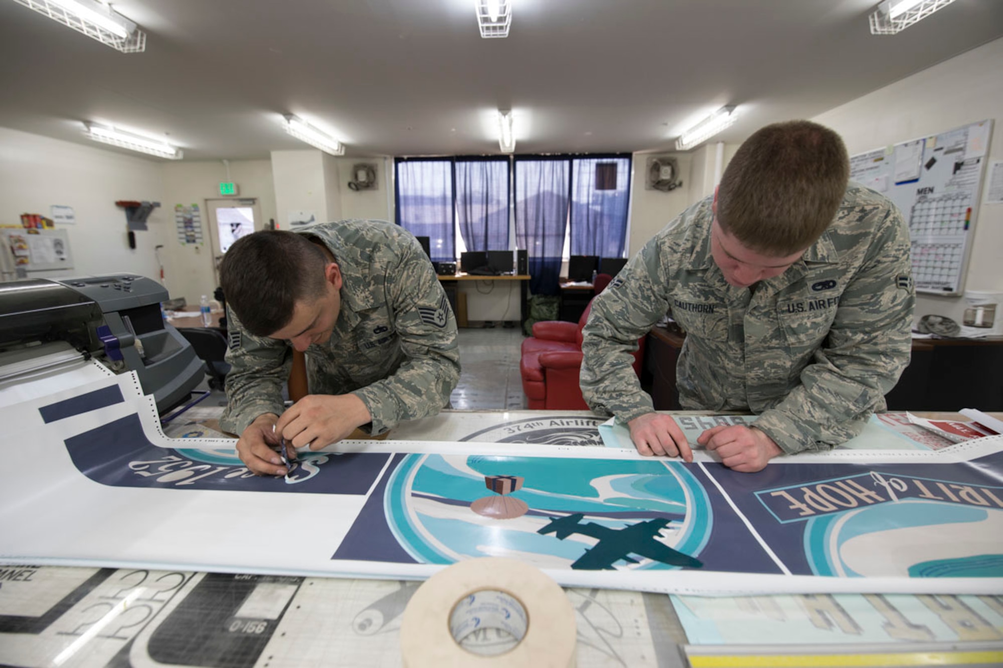 Staff Sgt. Jared Boles and Airman 1st Class Caleb Cauthorn, both with the 374th Maintenance Squadron aircraft structural maintenance, delicately remove excess vinyl from a newly printed nose art piece for a C-130J Super Hercules at Yokota Air Base, Japan, May 19, 2017. The nose art is printed on vinyl by select members of the fabrication shop, and carefully applied to the prepped surface of the aircraft. The digital approach took upwards of 30 hours to complete a project from sketch pad to prepress printing. (U.S. Air Force photo by Yasuo Osakabe)