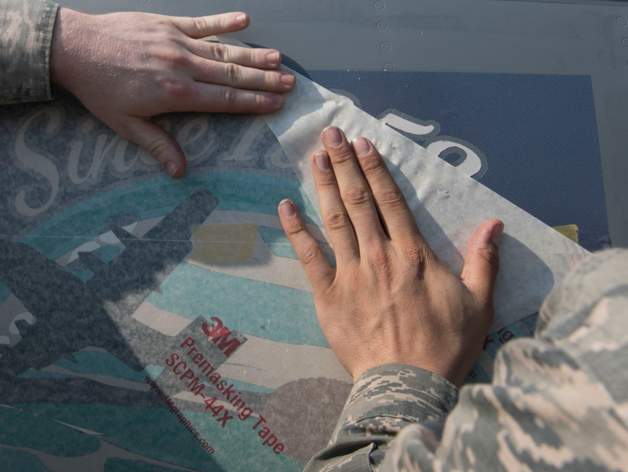Airman 1st Class Caleb Cauthorn and Staff Sgt. Jared Boles, both with the 374th Maintenance Squadron aircraft structural maintenance, carefully place decal of a C-130J airdrop over an island on the 3rd C-130J Super Hercules at Yokota Air Base, Japan, May 19, 2017. As a way to revitalize emphasis on heritage, the Air Force is bringing back nose art to select aircraft. The nose art was designed and donated by graphic artist Samantha Beaty. (U.S. Air Force photo by Yasuo Osakabe)