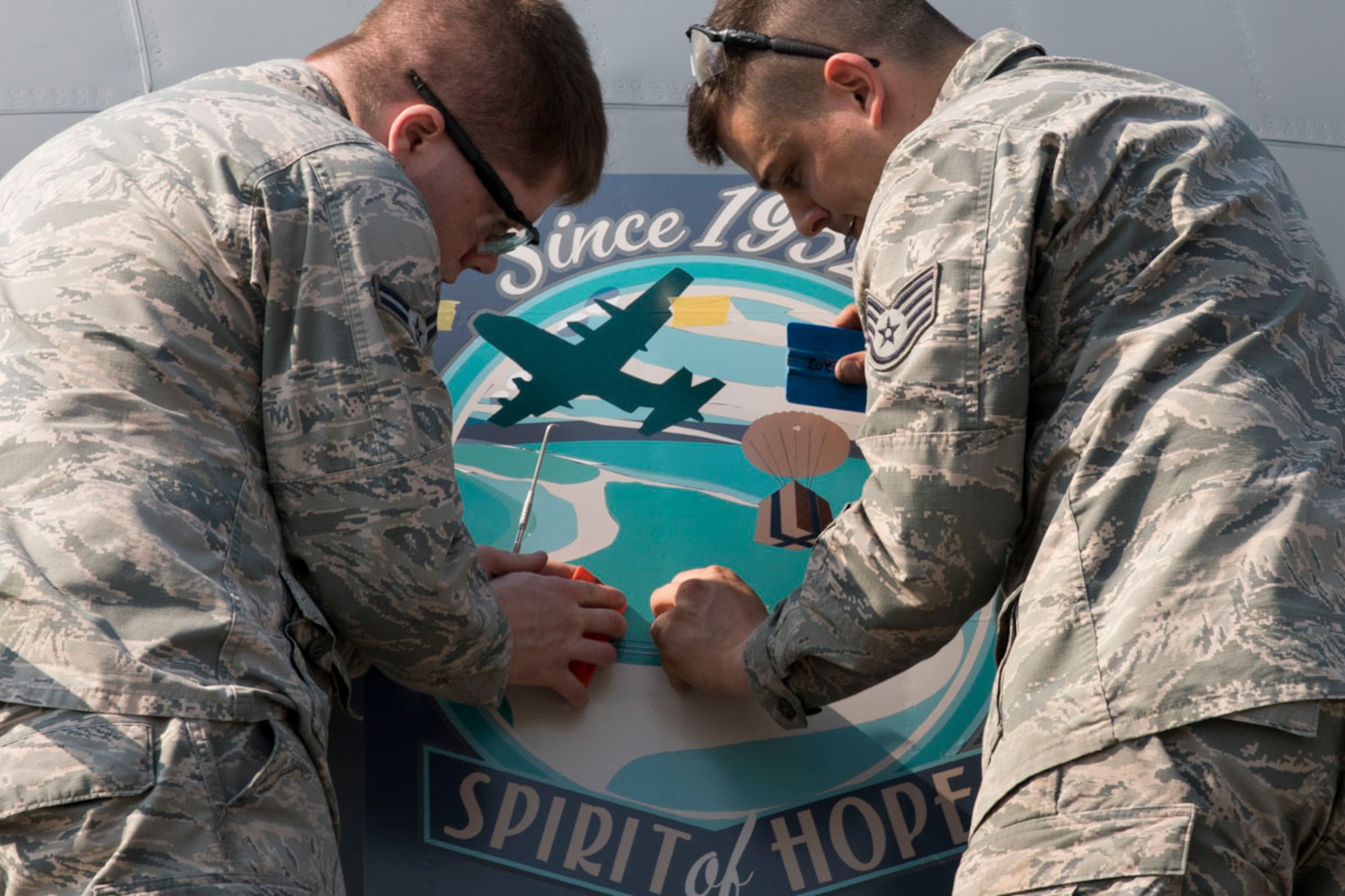 Airman 1st Class Caleb Cauthorn and Staff Sgt. Jared Boles, both with the 374th Maintenance Squadron aircraft structural maintenance, remove air bubbles from a decal placed on the side of C-130J Super Hercules 15-5813 at Yokota Air Base, Japan, May 19, 2017. The nose art design, "Spirit of Hope," which was designed and donated by graphic artist Samantha Beaty, celebrates the United States Air Force's dedication to providing humanitarian assistance and disaster relief to nations throughout the Indo-Asia-Pacific region. The artwork itself is a rendering of an Air Force C-130 airdropping humanitarian aid during Operation Christmas Drop. For 65 years running, Yokota Air Base aircraft and personnel have supported this event. In 2016 alone, four Yokota Air Base C-130s, along with the Royal Australian Air Force and Japan Air Self-Defense Force, airdropped 25 tons of aid to 25,000 people spread across 56 Micronesian islands. (U.S. Air Force photo by Yasuo Osakabe)