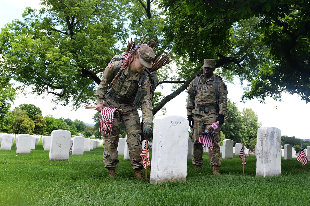 Army Pvt. Inem Uko, right, looks on while Army Sgt. Iwona Kosmaczewska places an American flag in front of a headstone during "Flags In" at Arlington National Cemetery in Arlington, Va., May 25, 2017. Uko and Kosmaczewska are combat medics assigned to the 3rd U.S. Infantry Regiment, known as "The Old Guard." DoD photo by Sebastian J. Sciotti Jr.        