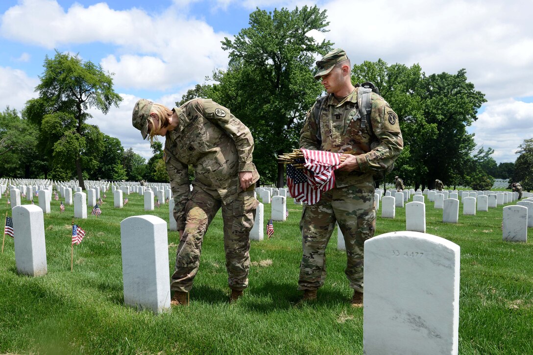 Army Capt. Eric Wagner, right, hold American flags, while Army Capt. Alli Thornton places an American flag in front of a headstone during "Flags In" at Arlington National Cemetery in Arlington, Va., May 25, 2017. Wagner is a physician assistant and Thornton is a physical therapist assigned to the 4th Battalion, 3rd U.S. Infantry Regiment, known as "The Old Guard." DoD photo by Sebastian J. Sciotti Jr.