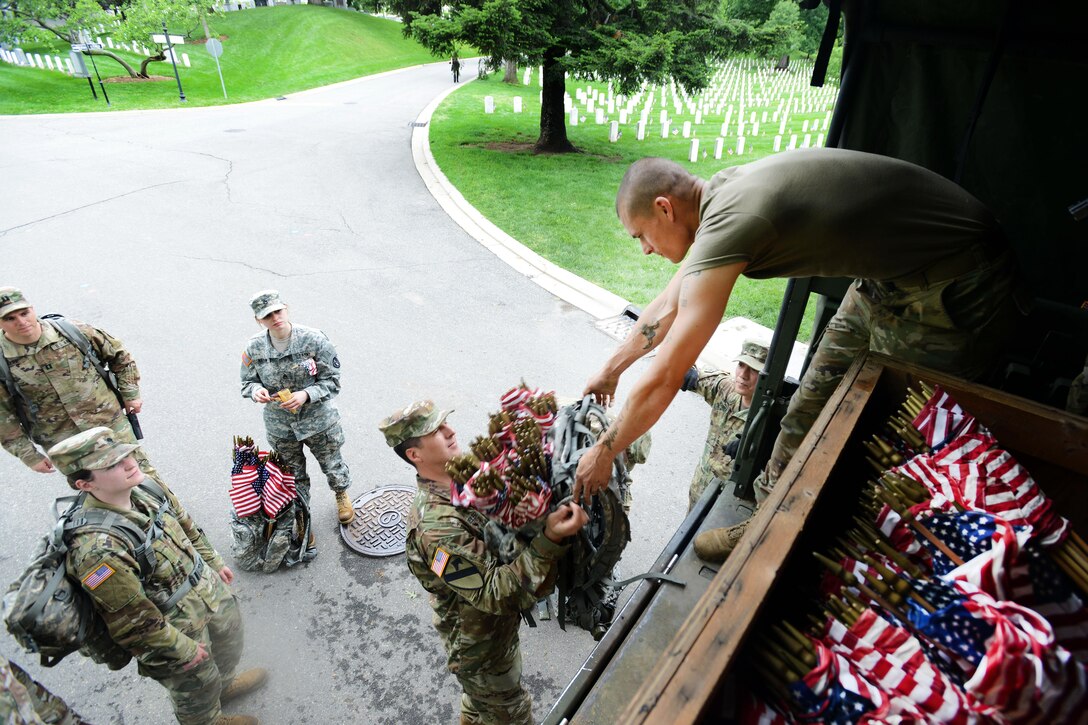 Army Maj. Anthony Freiler, center, receives a rucksack full of American flags from Army Sgt. Ryan Crittenden before moving out to place the flags in front of a headstone during "Flags In" at Arlington National Cemetery in Arlington, Va., May 25, 2017. Freiler is a doctor and Crittenden motor vehicle repairmen assigned to the 3rd U.S. Infantry Regiment, known as "The Old Guard." DoD photo by Sebastian J. Sciotti Jr.