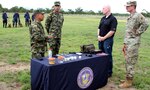 A Colombian military working dog handler and trainer briefs Lt. Col. Douglas Owens (black shirt), U.S. Army Medical Center & School Animal Medicine Branch chief, and Lt. Col. Troy Creason, (far right), U.S. Army South veterinarian, about demining training conducted in Tolemaida, Colombia, just before performing a demonstration. 