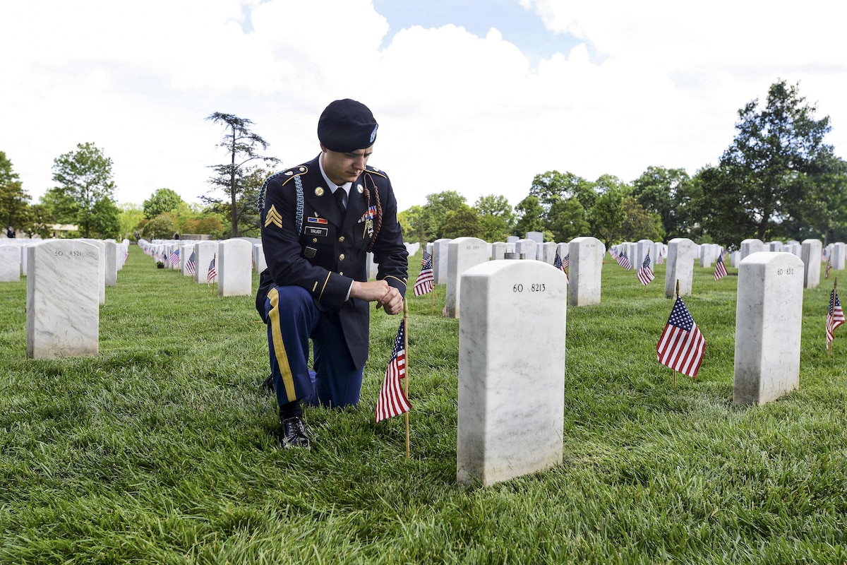 A soldier kneels as he pays respects to a close friend at a cemetery.