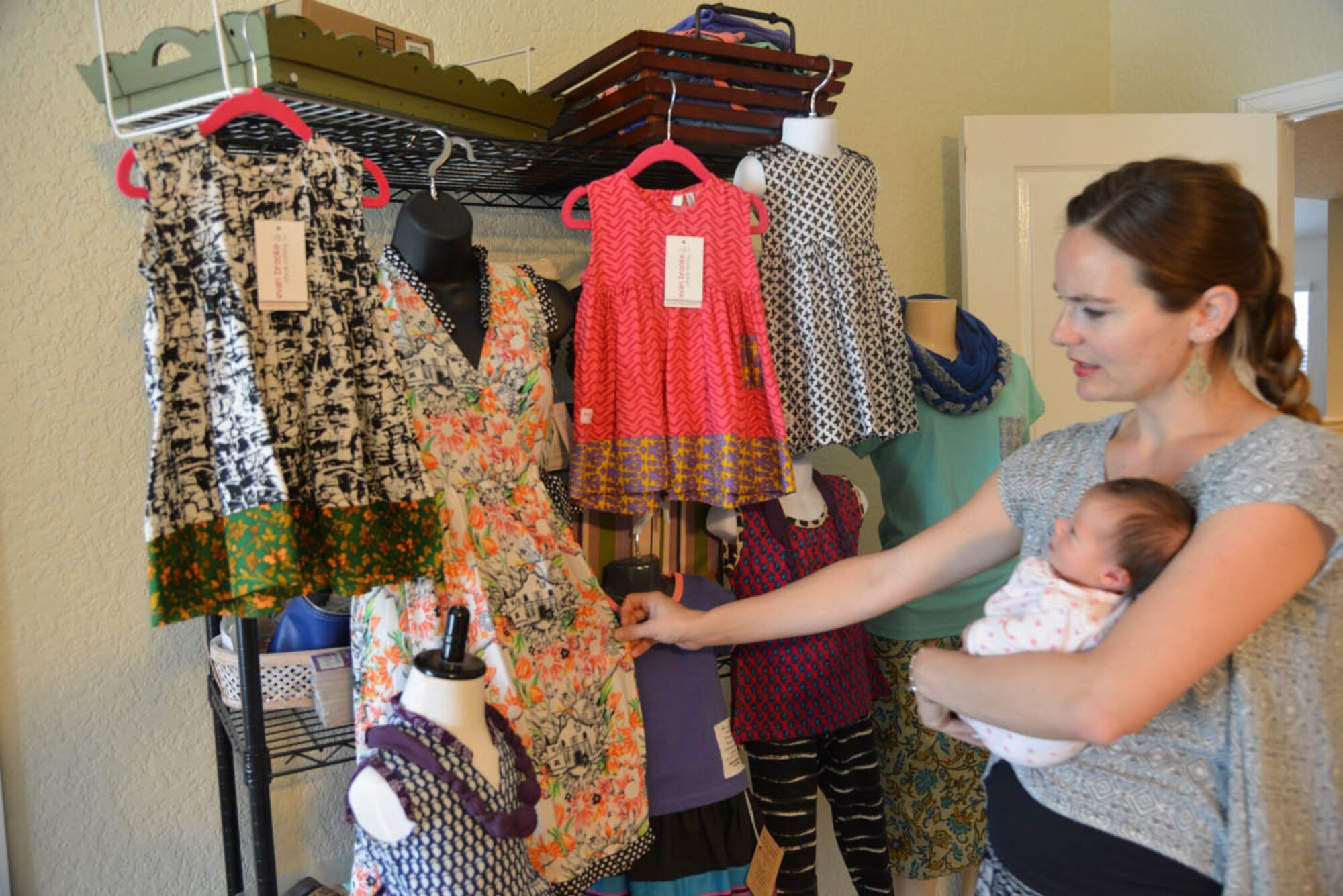 Evan Menendez, with her youngest child, Stevie, in her arms, display some of the designs for girls in the Evan Brooke’s Ethical Clothing inventory in her home, May 24, 2017.  The clothing line provides jobs and assistance to those affected by human trafficking. (U.S. Air Force photo by Minnie Jones)