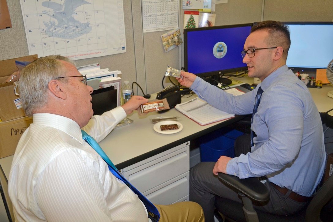 James Lecollier (left), Subsistence chief of individual rations branch, and Matt Conroy, Subsistence contract specialist, discuss sample products of a new performance bar that Army recruits will start receiving this summer. Conroy is in DLA’s Pathways to Career Excellence program and helped procure the bars. 