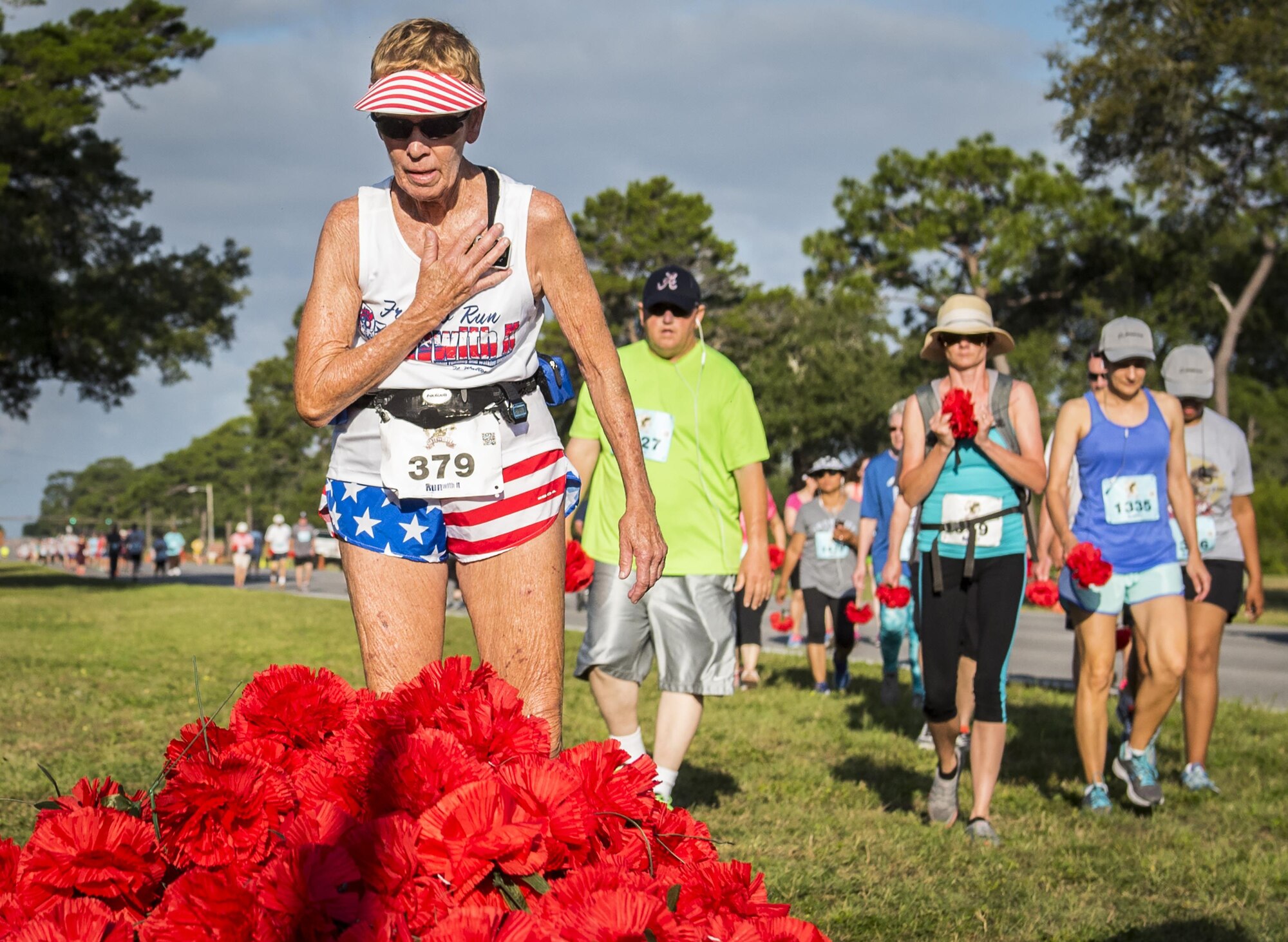 Mary Newcomer stops for a moment of silence at the All Wars Memorial as other runners approach with red carnations during the 32nd annual Gate to Gate run at Eglin Air Force Base, Fla., May 27.  More than 900 people participated at this year’s event.  (U.S. Air Force photo/Samuel King Jr.)