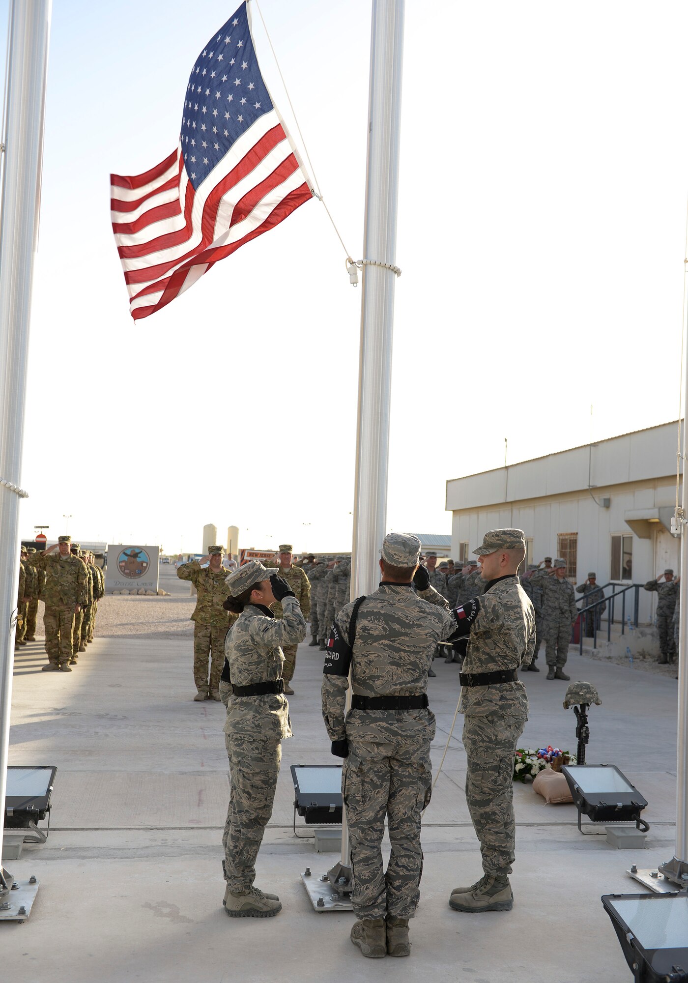 Members of the 379th Air Expeditionary Wing Honor Guard lower the flag as military members stand in salute at Al Udeid Air Base, Qatar, May 29, 2017. The formation was part of a Memorial Day Retreat Ceremony held in honor of those who have died while in military service. (U.S. Air Force photo by Tech. Sgt. Bradly A. Schneider/Released)