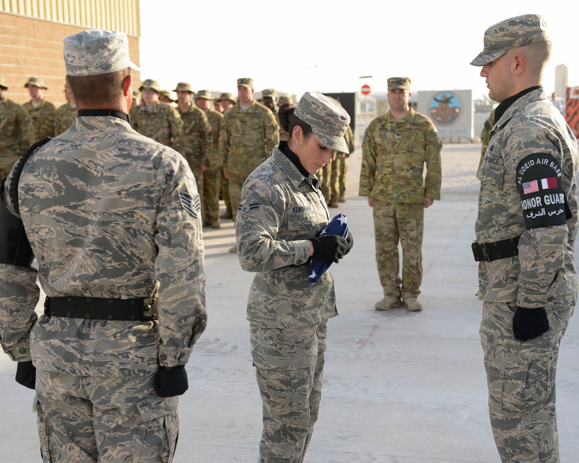 U.S. Air Force Airmen 1st Class Jessica Kornmann, 379th Air Expeditionary Wing Honor Guard, folds the American Flag while fellow Honor Guard members as well as members from Al Udeid Air Base stand in salute at Al Udeid Air Base, Qatar, May 29, 2017. The flag retirement was part of a Memorial Day Retreat Ceremony held in honor of those who have died while in military service. (U.S. Air Force photo by Tech. Sgt. Bradly A. Schneider/Released)