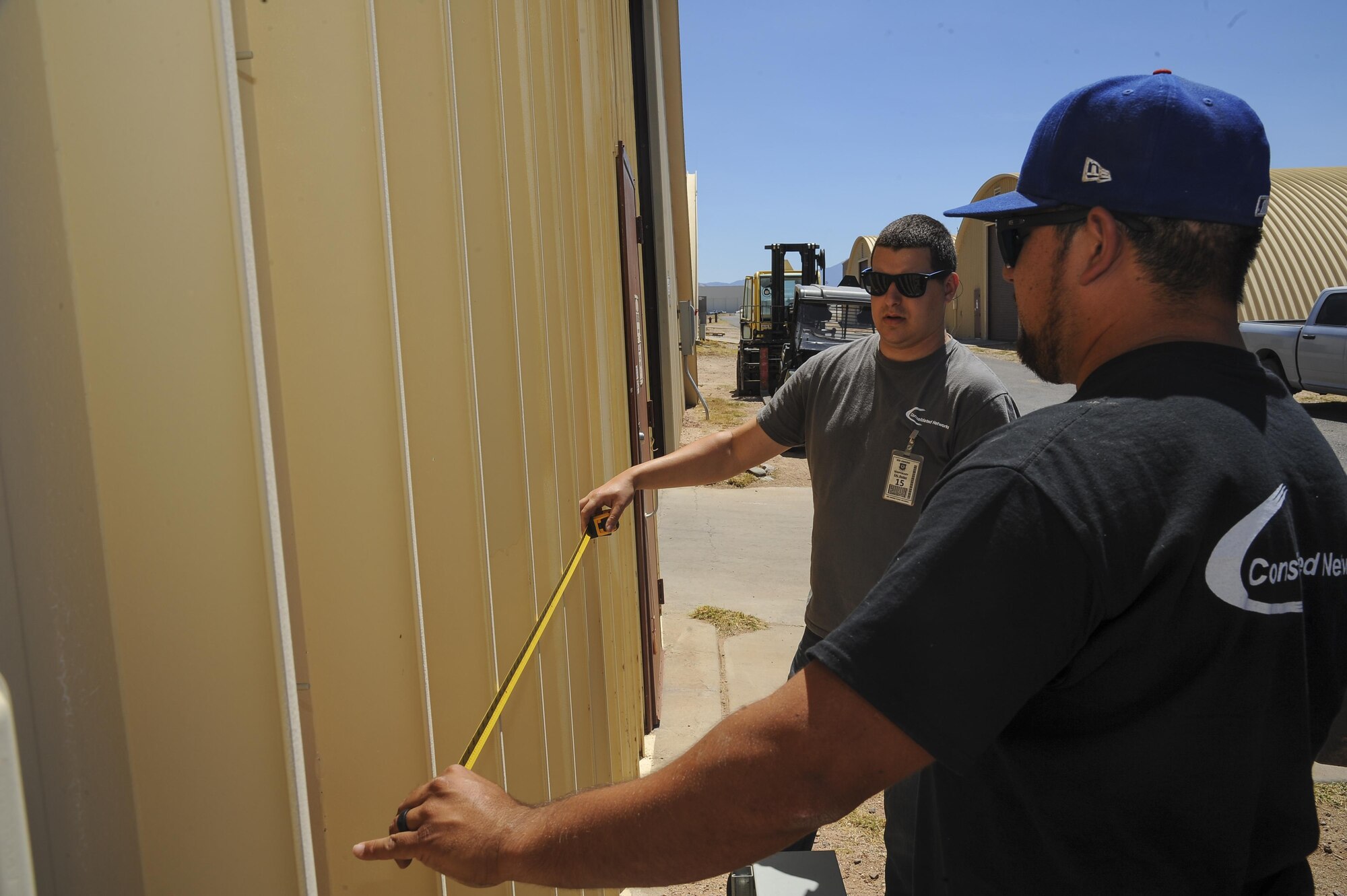 Brodie Carrier and Mark Webber, Consolidated Networks fiber technicians, take measurements for a bracket for a communications cabinet installation at the 309th Aircraft Maintenance and Regeneration Group at Davis-Monthan Air Force Base, Ariz., May 24, 2017. The contractors and 355th Communications Squadron Airmen have been in the process of creating and executing a modification plan, upgrading D-M’s network without interfering with any of the Desert Lightning Team’s connectivity. (U.S. Air Force photo by Senior Airman Mya M. Crosby)