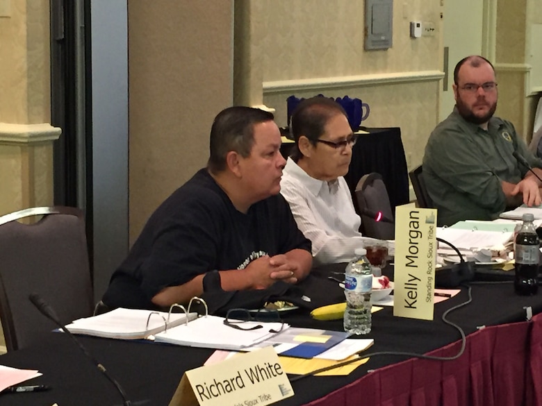 Two women and one man seated at a table.  One woman is speaking into a microphone.