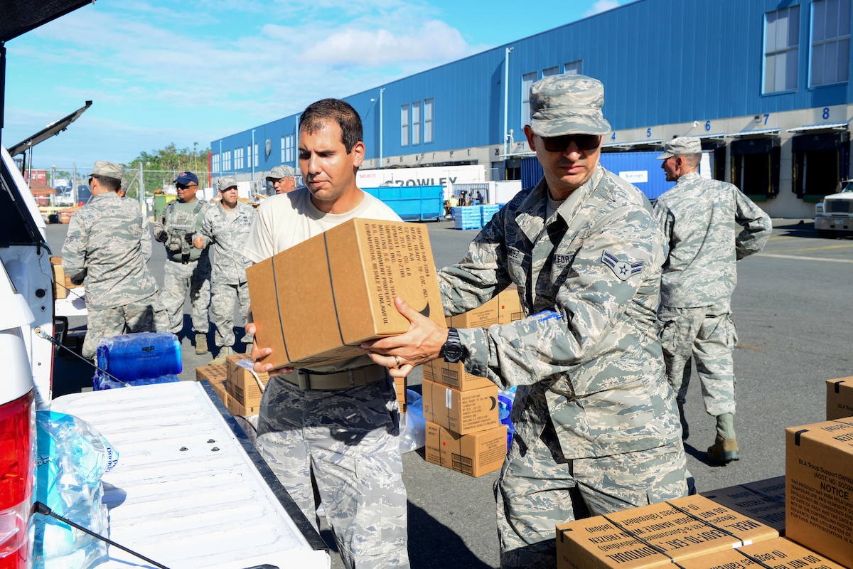 A line of airmen load boxes into the back of a car.