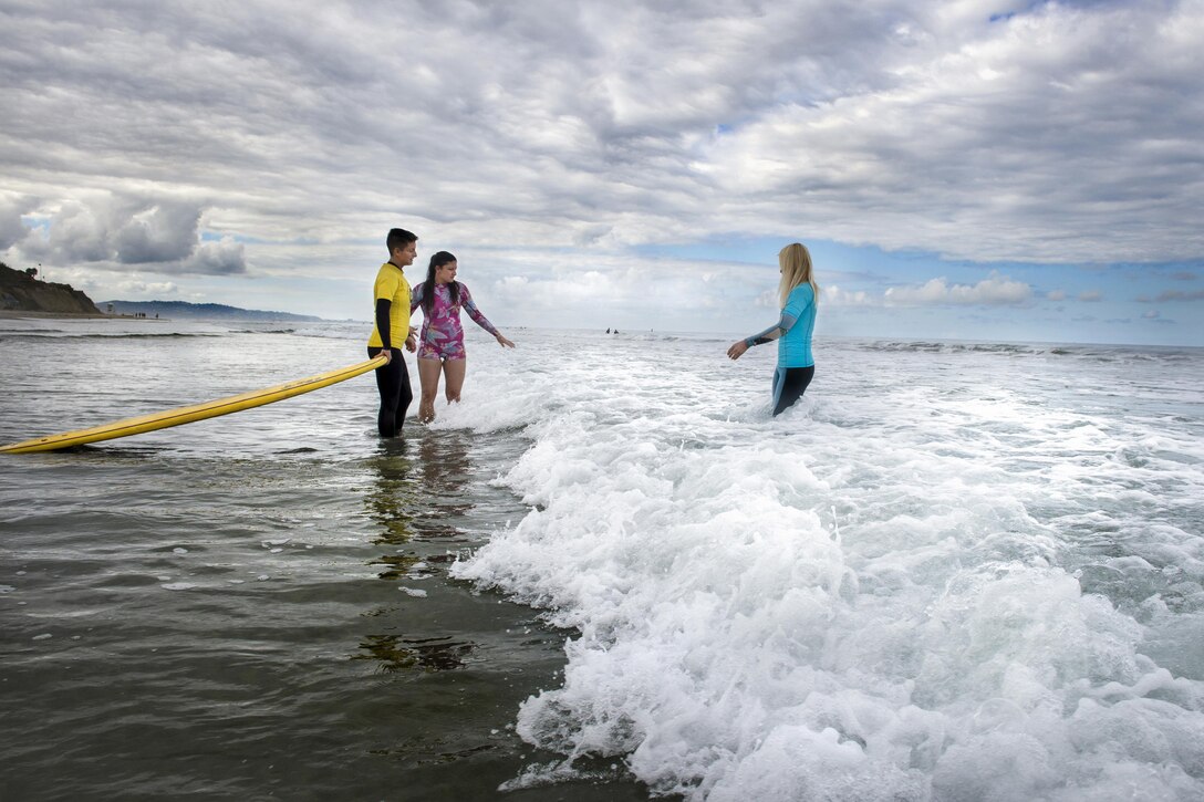 A surfer is assisted by a volunteer as she enters the water to meet a surfing instructor.