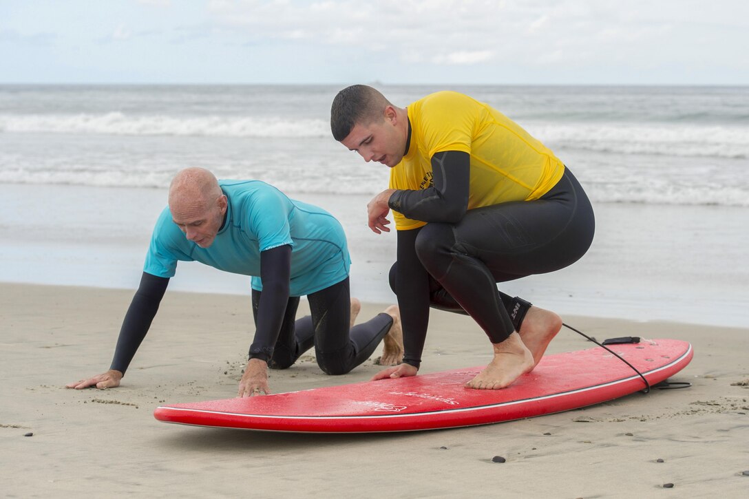 An instructor gives tips to a surfer who's on a surfboard on the beach.