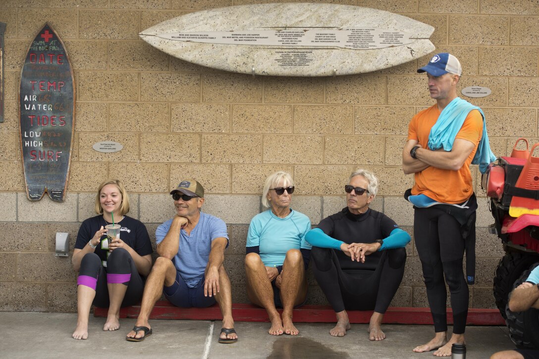 Volunteers stand and squat against a wall while listening to a brief before a surf therapy session.