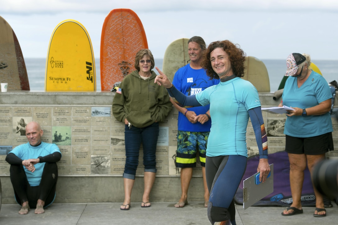 A program manager points out safety measures while standing with a group of surfers.