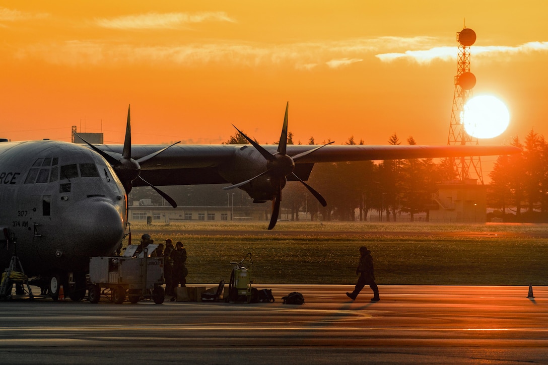 A service member walks towards an aircraft with the sun in the background.