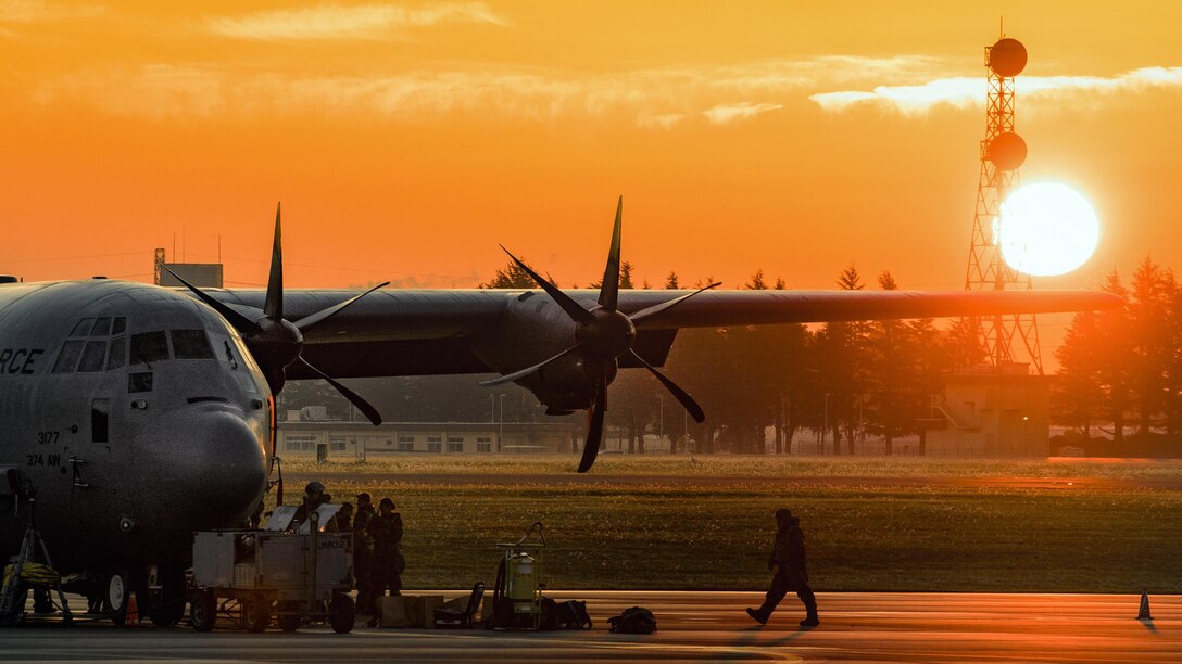 A service member walks towards an aircraft with the sun in the background.