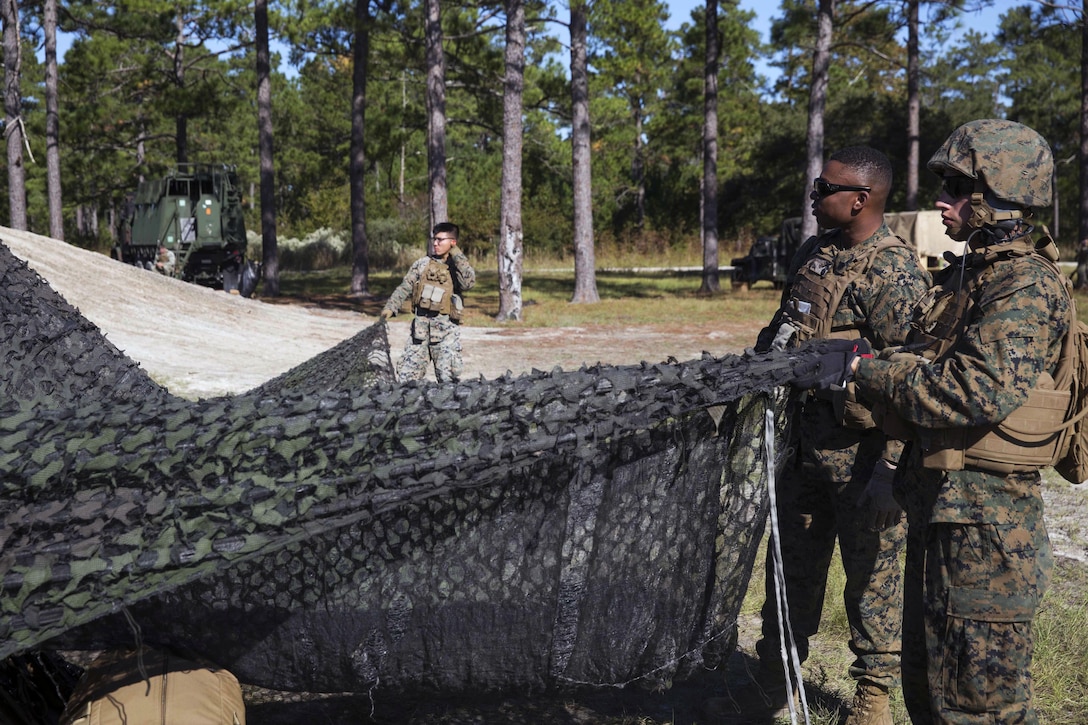 Three Marines drape a net over a vehicle.