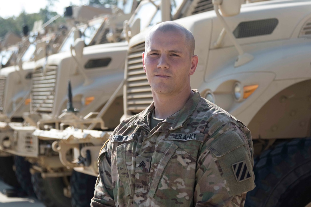 Soldier poses in front of military vehicles.