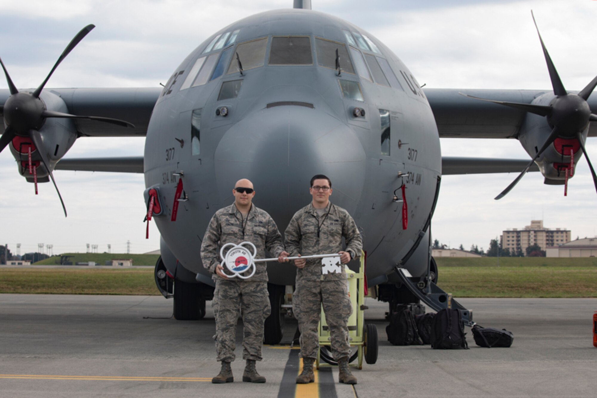 Staff Sgt. James Duncan and Senior Airman Ian Hall, both from the 374th Aircraft Maintenance Squadron crew chiefs, pose for a photo in front of a C-130J Super Hercules at Yokota Air Base,  Japan, Oct. 31, 2017. This is the sixth C-130J delivered to Yokota and the first from Dyess Air Force Base, Texas, as part of fleet-wide redistribution of assets set in motion by Air Mobility Command.