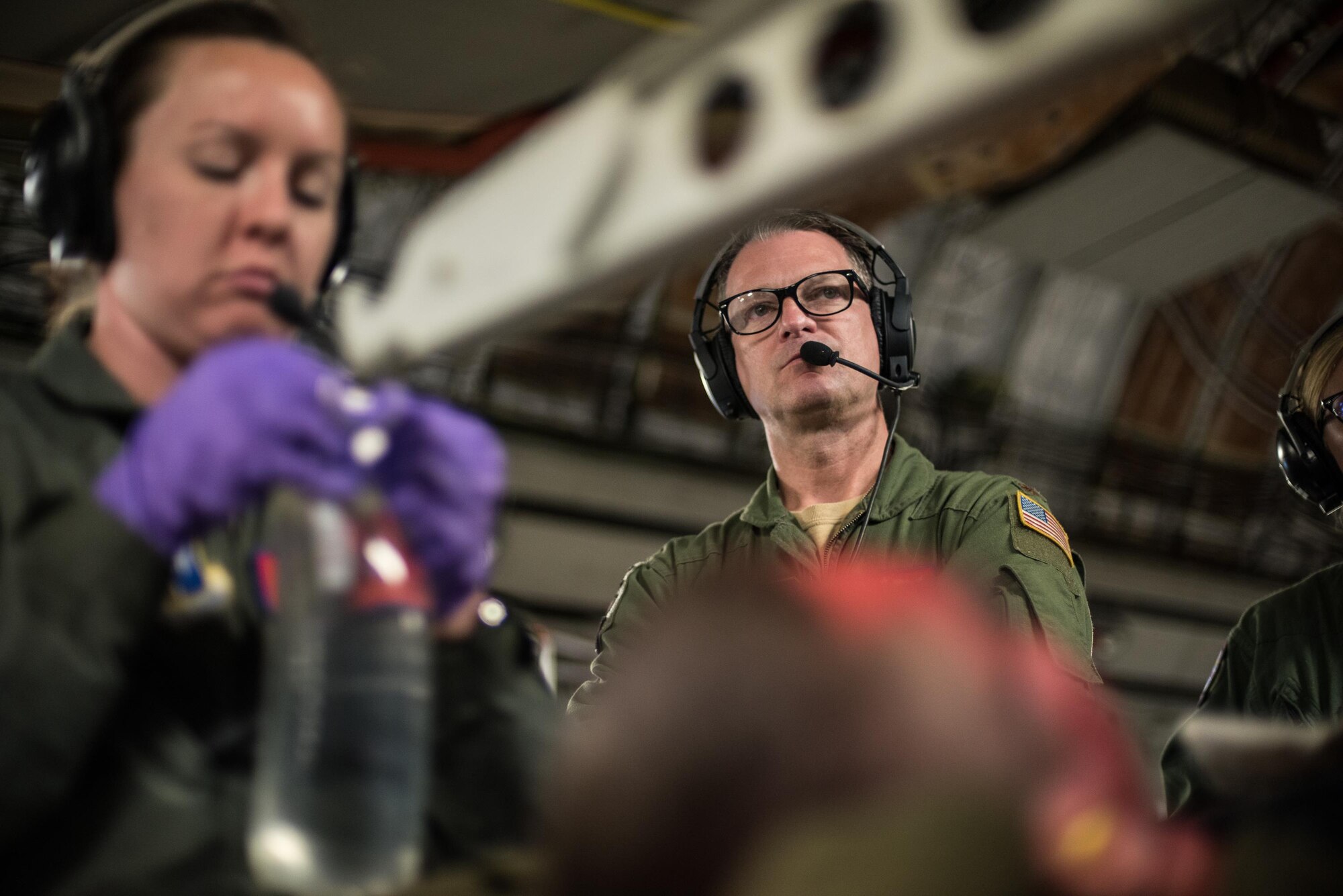 Maj. Casey Patton, medical crew coordinator for the flight and senior health technician at the 137th Aeromedical Evacuation Squadron, Will Rogers Air National Guard Base, Oklahoma City, listens to a crew member through his headset as another aeromedical technician hangs an IV fluid bag while transporting simulated burn patients aboard a C-17 Globemaster III from the 105th Airlift Wing, Stewart Air National Guard Base, N.Y., en route to Altus Air Force Base, Altus, Okla., Oct. 30, 2017. The flight was part of a wildfire scenario during Vigilant Guard, a North American Command-sponsored, state-wide emergency response exercise held Oct. 30 to Nov. 2, 2017. (U.S. Air National Guard photo by Staff Sgt. Kasey M. Phipps)