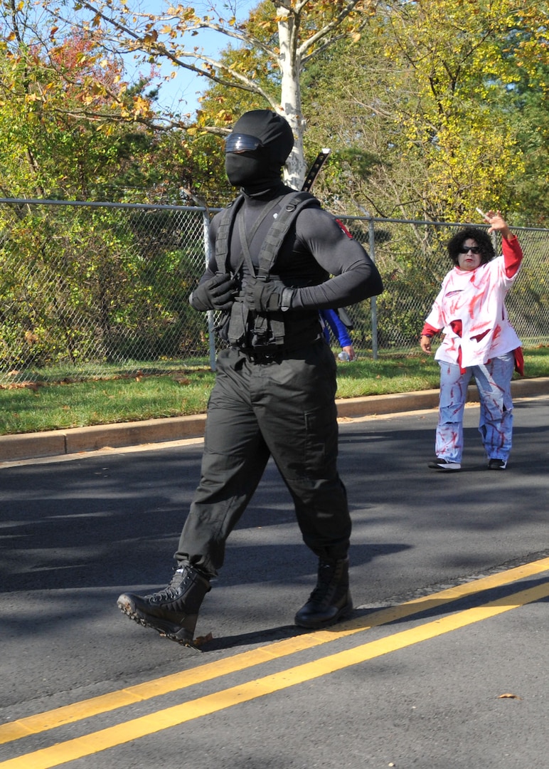 A man dressed in all black as a ninja and a woman dressed as a zombie walk down a road