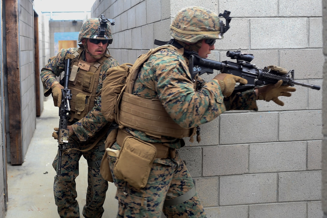 Two Marines creep around a corner with guns during a training exercise.