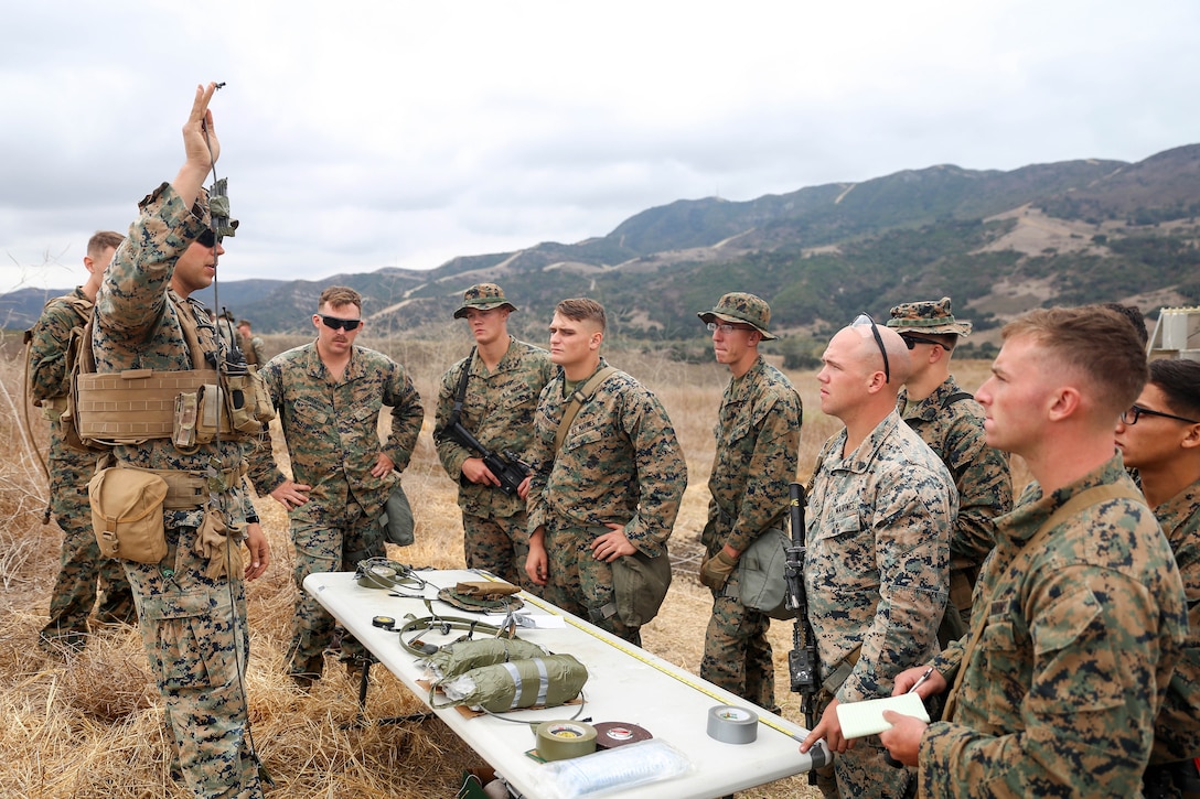 Marines stand around a table listening to a briefing.