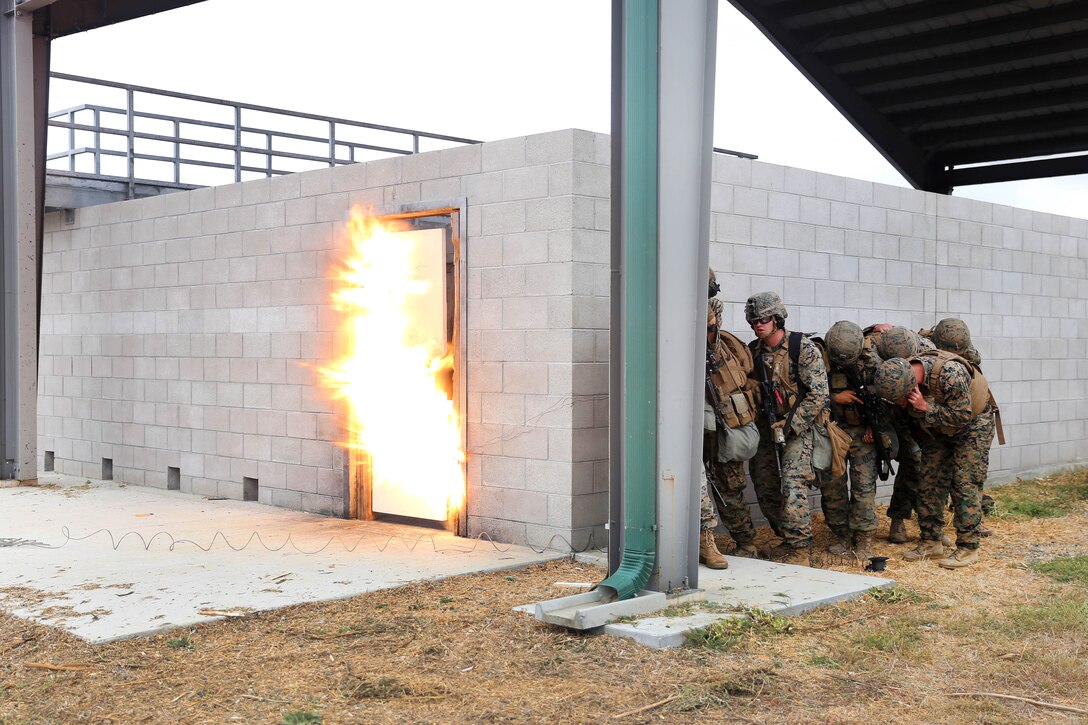 Marines take cover behind a wall during an explosion.