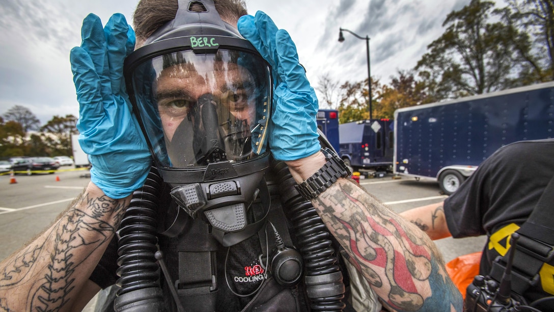 A solider with gloves adjusts a breathing mask.