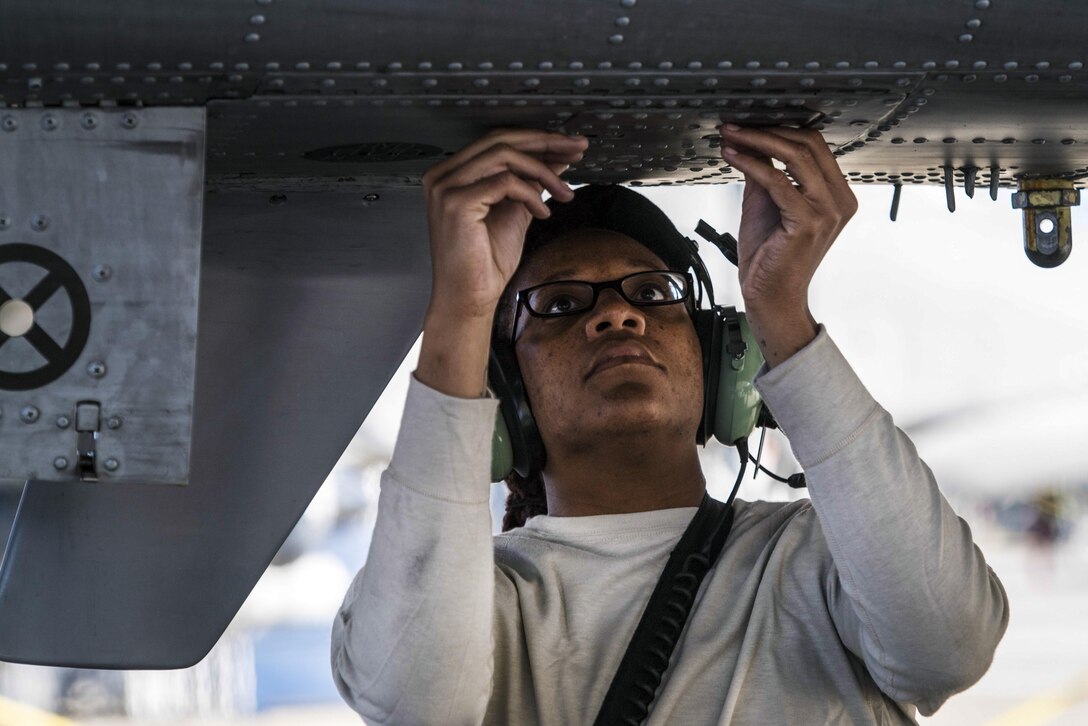 An airman works on the underbelly of an airplane.