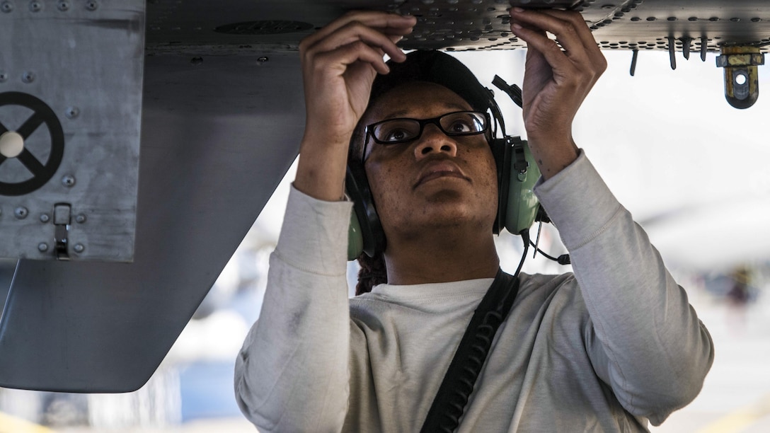 An airman works on the underbelly of a airplane.