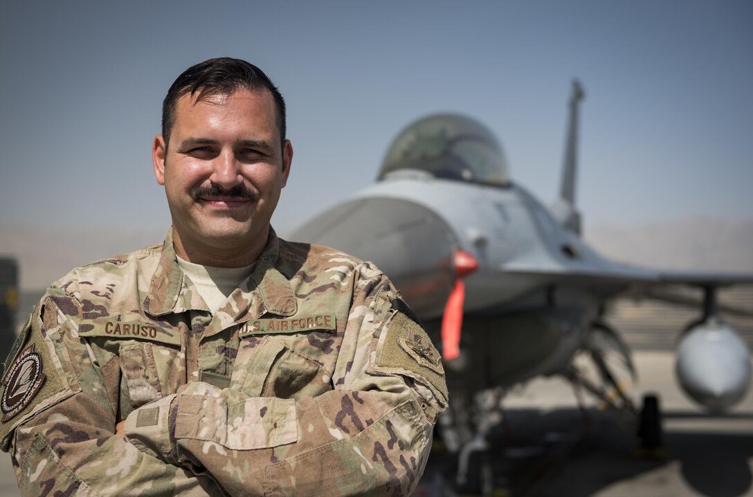Airman poses for a photo in front of an F-16 fighter jet.