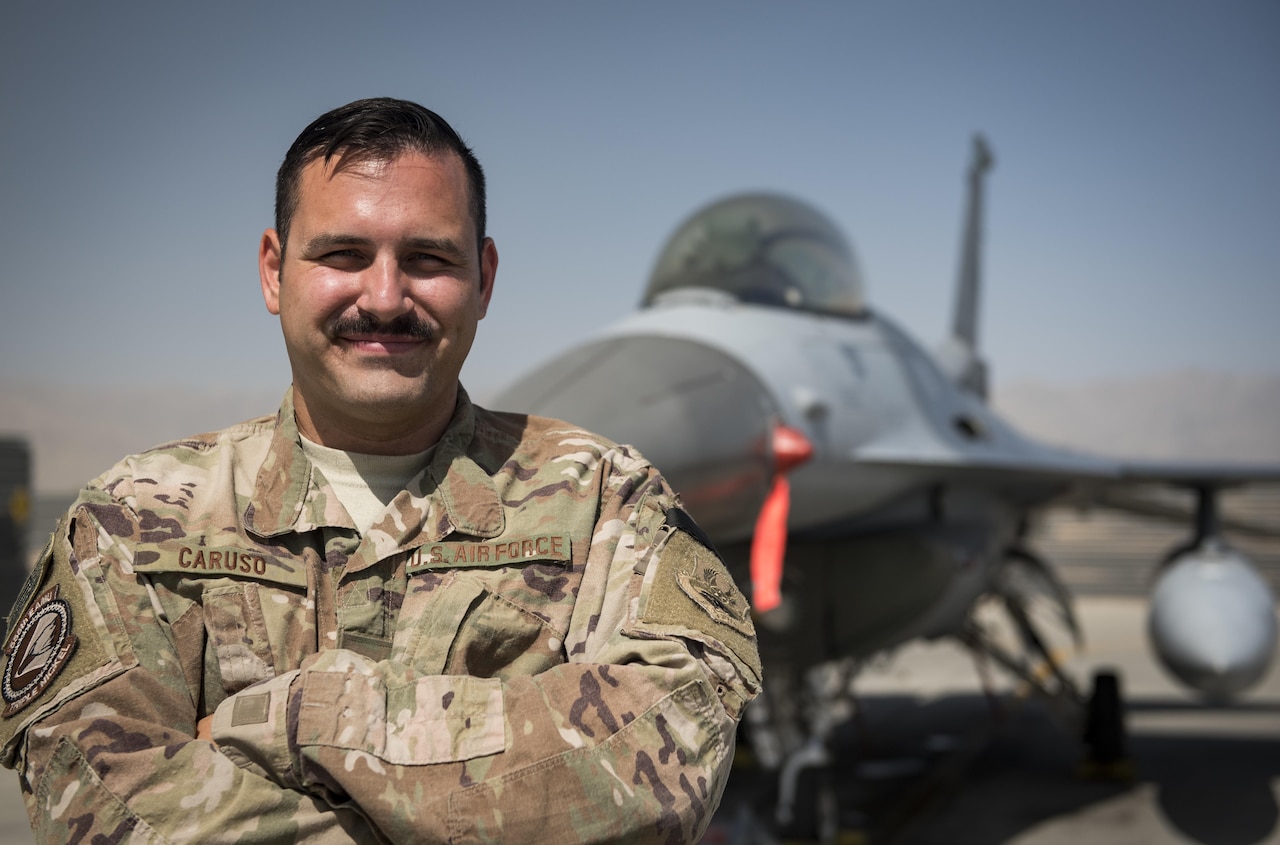 Airman poses for a photo in front of an F-16 fighter jet.